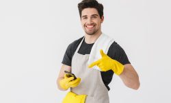 Handsome brunette houseman wearing apron standing isolated over white background, showing mobile phone